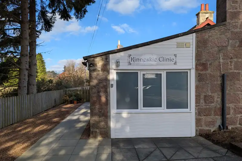 Wooden extension to a red granite building, signposted as the Kinneskie Clinic